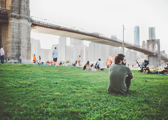 man-sitting-on-green-lawn-under-bridge